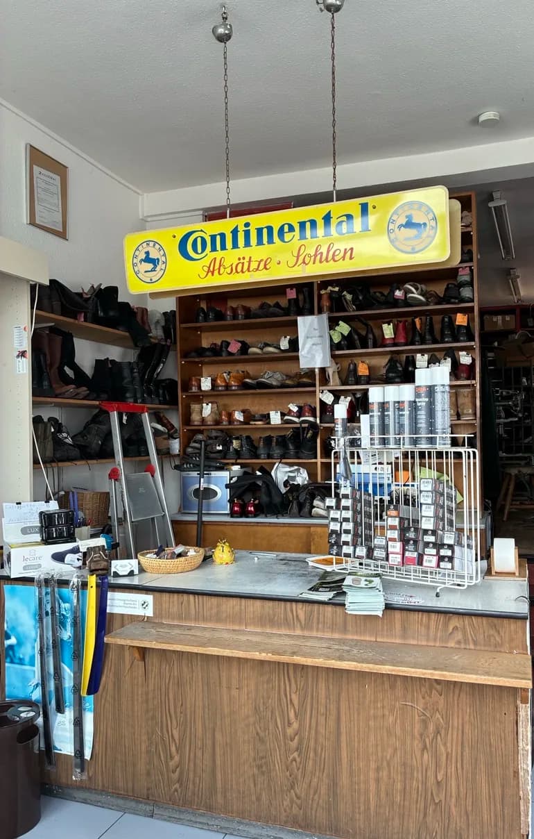 Verkaufsraum der Schuhmacherei Zunner in der Maxfeldstraße mit Holztheke, Regalen voller Schuhe und dem alten Continental-Schild „Absätze · Sohlen“